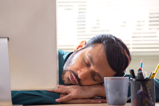 A corporate employee in formal clothing sleeping behind desktop in office.
