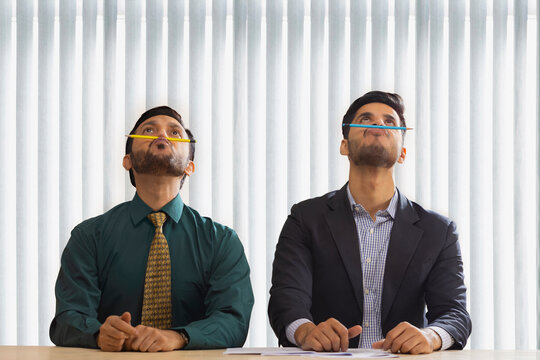 Corporate co-workers sitting together and balancing pencils on their nose.