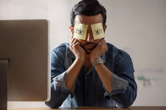 A corporate employee sitting with eyes covered with sticky notes in front of his desktop.