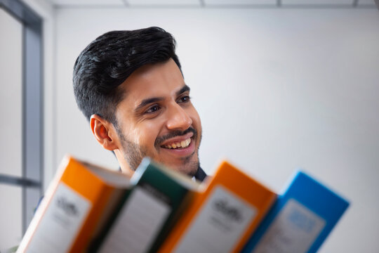 A corporate employee's smiling face behind office files.