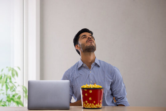 A happy corporate employee in formal clothing sitting with a laptop eating popcorn.