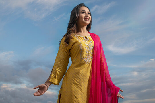 Happy woman in yellow salwar standing under the blue sky with her arms outstretched