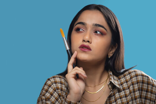 Young artist girl thinking for a new idea with holding brush in hand and hand on cheek