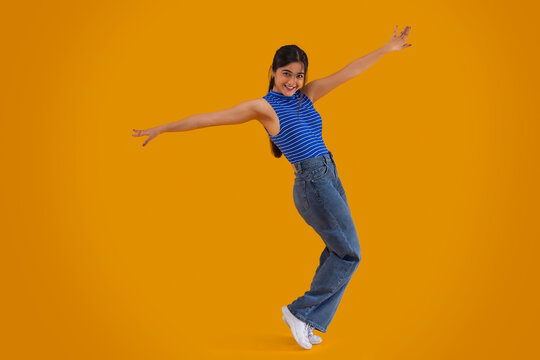 Portrait of a young girl standing on toes with her arms outstretched in front of the camera