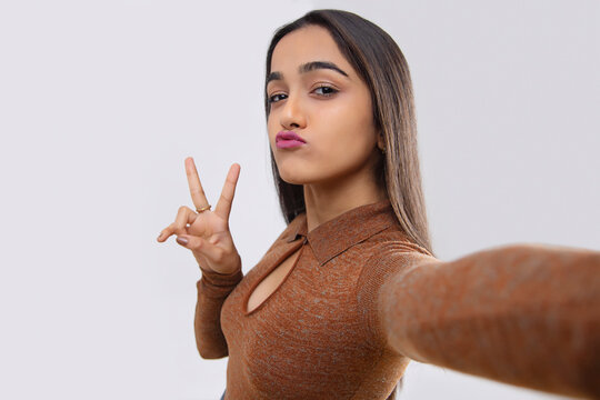 Young girl showing duck face and peace gesture while taking selfie