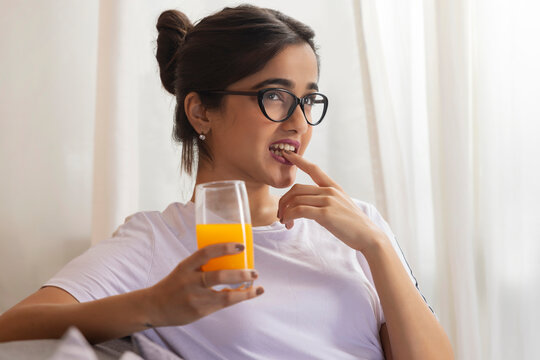 Beautiful girl looking away and thinking while sitting at home with a glass of juice