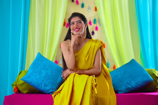 Indian bride in yellow saree sitting on stage with hand on chin 
