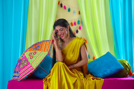 Indian bride in yellow saree sitting on stage and smiling with hand on forehead
