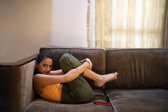 A young woman crouching on her couch in room while looking at the camera.