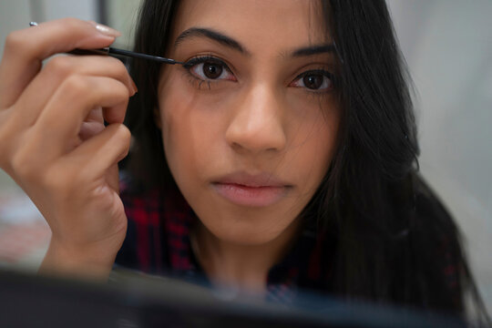 A young woman applying eyeliner on her lids with a wand in her hand.