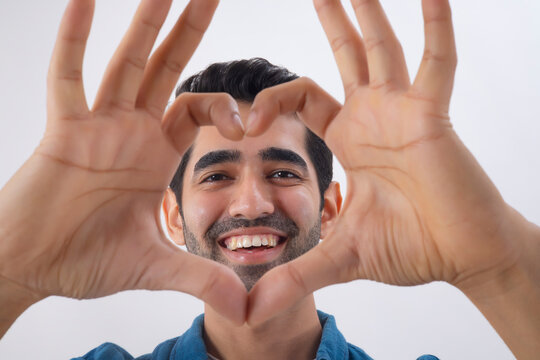 Adult man forming heart shape with her fingers and looking at camera through it