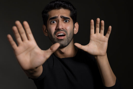 Portrait of a frightened young man looking at the camera and gesturing with his hands