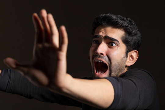 Portrait of a frightened young man looking away,raising hand and shouting 
