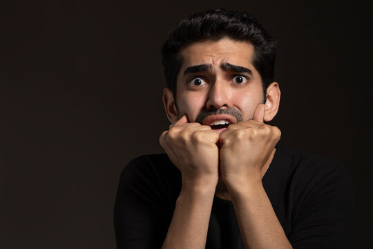 Portrait of a frightened young man looking  with big eyes and holding face with his hands