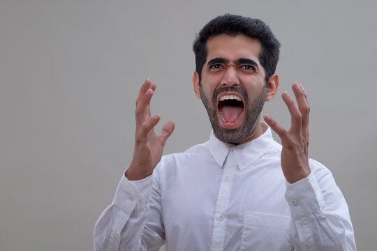 Portrait of an angry young man in white shirt shouting with raising his hands