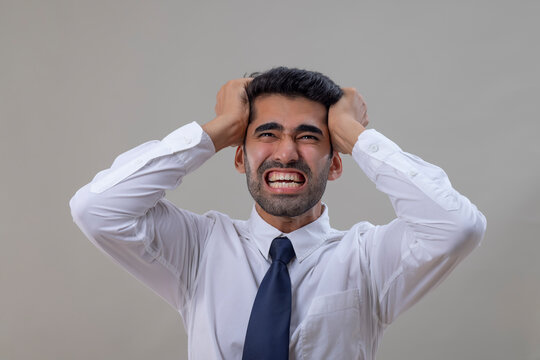 An angry young man in a white shirt pulling  his hair with both hands and shouting