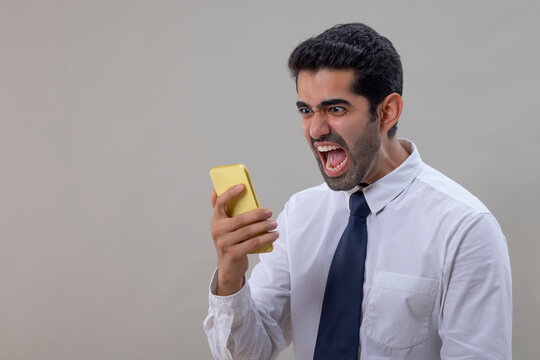 An angry young man in a white shirt shouting while talking on Smartphone