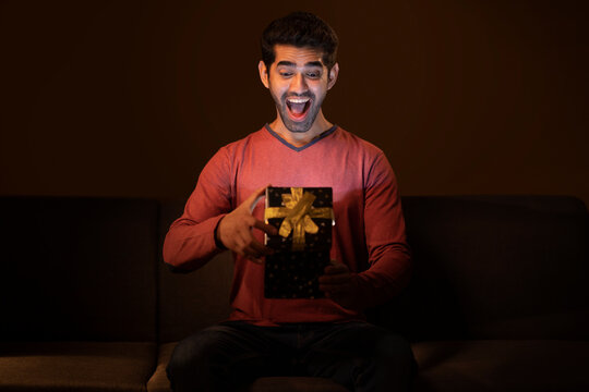 Happy young man unpacking gift box with curiosity