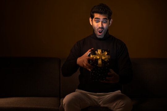 Happy young man unpacking gift box with curiosity