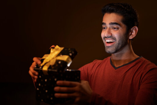 Happy young man unpacking gift box with curiosity