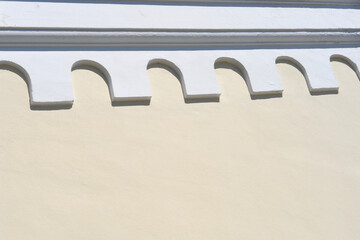 Fototapeta premium A wide horizontal shot captures a beige plaster wall featuring a decorative white geometric frieze pattern casting sharp shadows under bright sunlight