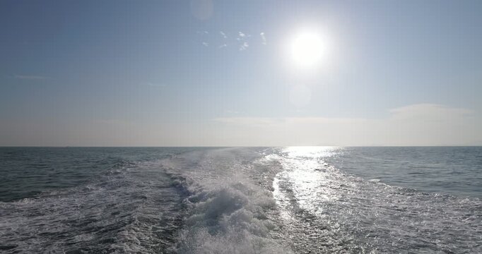 Looking back from old ferry boat sailing in early morning from Tioman island to mainland, slow motion shot. Bright sun on sky, white water splashes, long trail on calm sea water behind