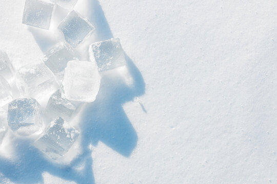 Crystal clear ice cubes on a natural snowy surface. Light blue tones background.