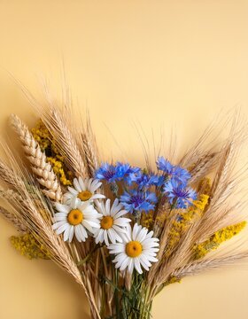 Bunch of flowers: blue coneflowers, daisies and yellow wheat ears on pale yellow background with copy space