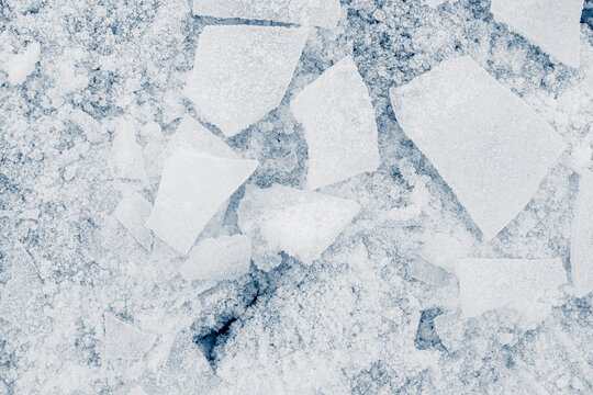 The texture of cracked ice, covered with snow. Shards of crushed thin ice in light blue tones. Background texture.