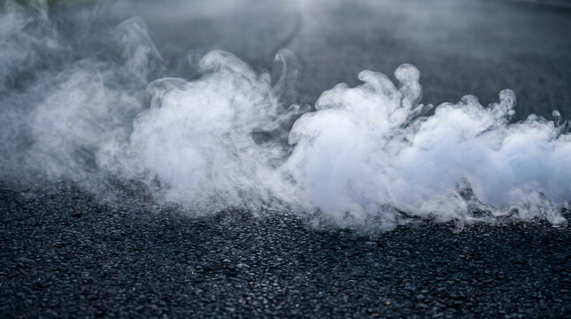 Humo denso y oscuro se desplaza sobre un suelo mojado y brillante, iluminado por un fuerte contraluz que crea un ambiente misterioso, dram&aacute;tico y cinematogr&aacute;fico.