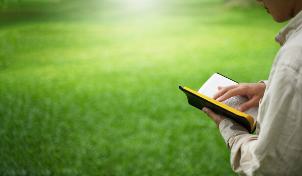 The concept of reading the Bible and praying to God for blessings, living peacefully in nature and spending time with God, with a hand holding a Bible.