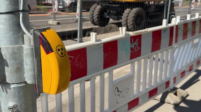 Close-up of a pedestrian crossing button near a road construction site with temporary barriers. Concept of pedestrian safety, traffic management, accessibility and urban infrastructure.