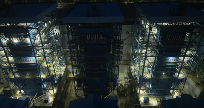 Aerial view of industrial factory boilers illuminated at night, showing heavy machinery and structural scaffolding.