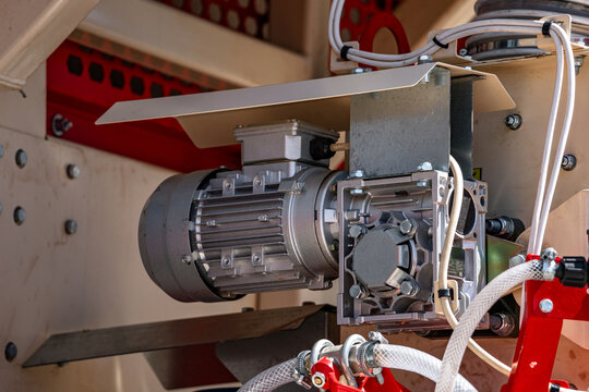 Agricultural machinery electric motor gearbox drive mechanism. Modern farm machine worm gear speed reducer component closeup view with protective shield and industrial technical engineering details.