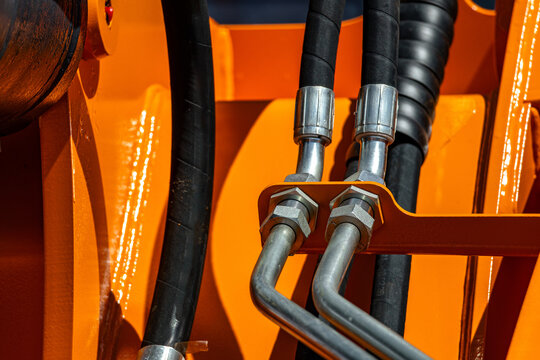 Agricultural tractor hydraulic hoses and steel pipe connections. Heavy machinery fluid power lines with threaded fittings on yellow frame and vehicle transport engineering closeup details.
