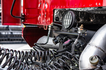 Fototapeta premium Semi truck pneumatic brake spiral hoses and work light closeup. Heavy duty commercial transport vehicle electrical connectors behind red cabin and long haul lorry mechanism engineering details.