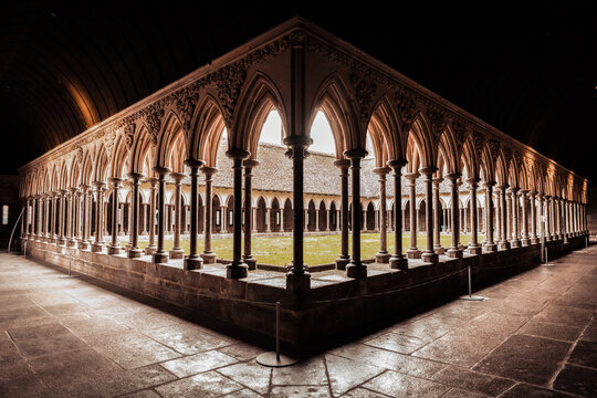 View of the illuminated Gothic cloister gallery at Le Mont-Saint-Michel Abbey in Normandy, France. Elegant medieval stone arches, dramatic perspective and atmospheric one of Europe.