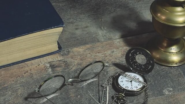 Man places antique glasses on a desk with a book, lamp, and pocket watch