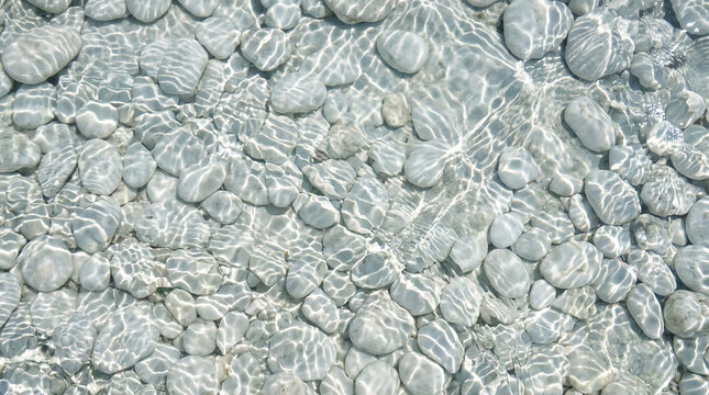 Clear water flows over smooth, rounded gray stones, creating shimmering light patterns on the riverbed.
