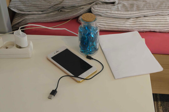 Smartphone charging on a table next to jars and papers in a simple room setting