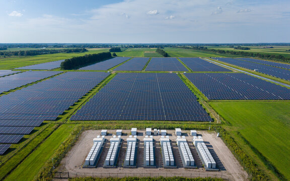 Aerial view of a large-scale solar farm featuring extensive rows of photovoltaic panels and a battery energy storage system in the rural landscape of Wanneperveen, Overijssel, Netherlands.