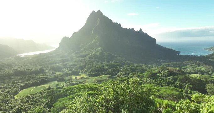 Sunlit French Polynesia mountains and lush jungle with sunrays and blue sky.
