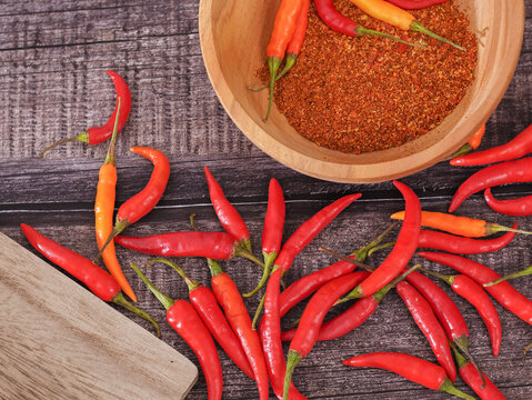 Ground red chili powder in a wooden bowl with fresh red chili peppers on a wooden cutting board over a rustic burlap background. Spicy seasoning ingredient for cooking with copy space.