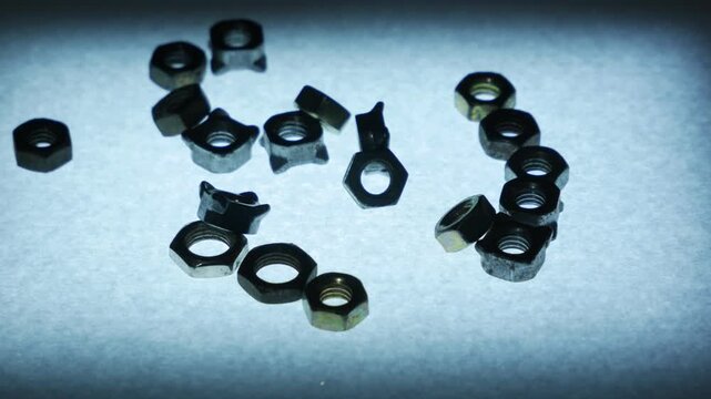 Hand Dropping Several Small Metal Hex Nuts onto Textured Surface