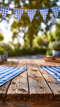 Rustic wooden plank table with two blue and white checkered gingham napkins, ready for an outdoor garden party or summer picnic beneath decorative bunting flags