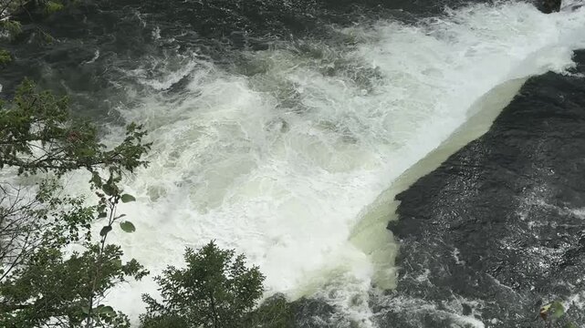 Upper Mesa Falls in Idaho, showing a powerful waterfall on the Henrys Fork of the Snake River surrounded by dense forest and volcanic canyon walls. The scene features rushing white water, mist rising.