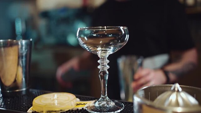 Empty cocktail glass with bartender preparing drink behind bar, Barman mixing beverage behind stemmed glass on counter with shaker 4k