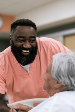 Smiling male caregiver engaging with elderly patient in hospital room for senior care background and nursing banner