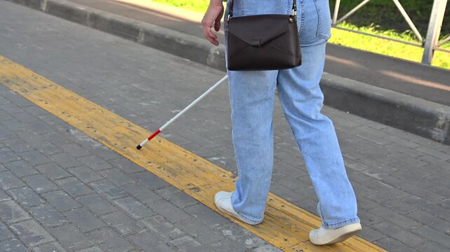 A blind woman walks on tactile paving. Close-up of her feet and a walking stick.