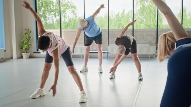 Diverse senior adults performing windmill stretching exercises in fitness studio. Clip is ideal for promoting active aging, senior wellness programs, and healthy lifestyle choices